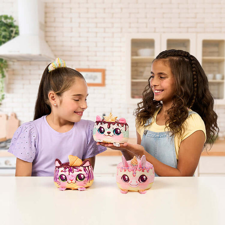 Two girls playing with Cookeez Makery Freezy Cakez Playset surprise plush toys in a kitchen setting.